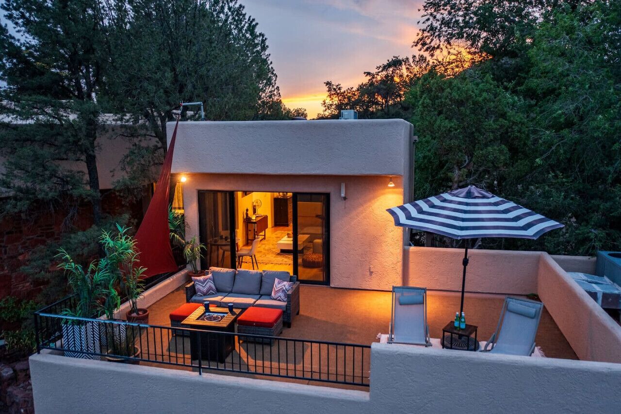 Un espace de vie extérieur moderne comprenant un ensemble de canapés, une table à manger et un parasol à rayures.