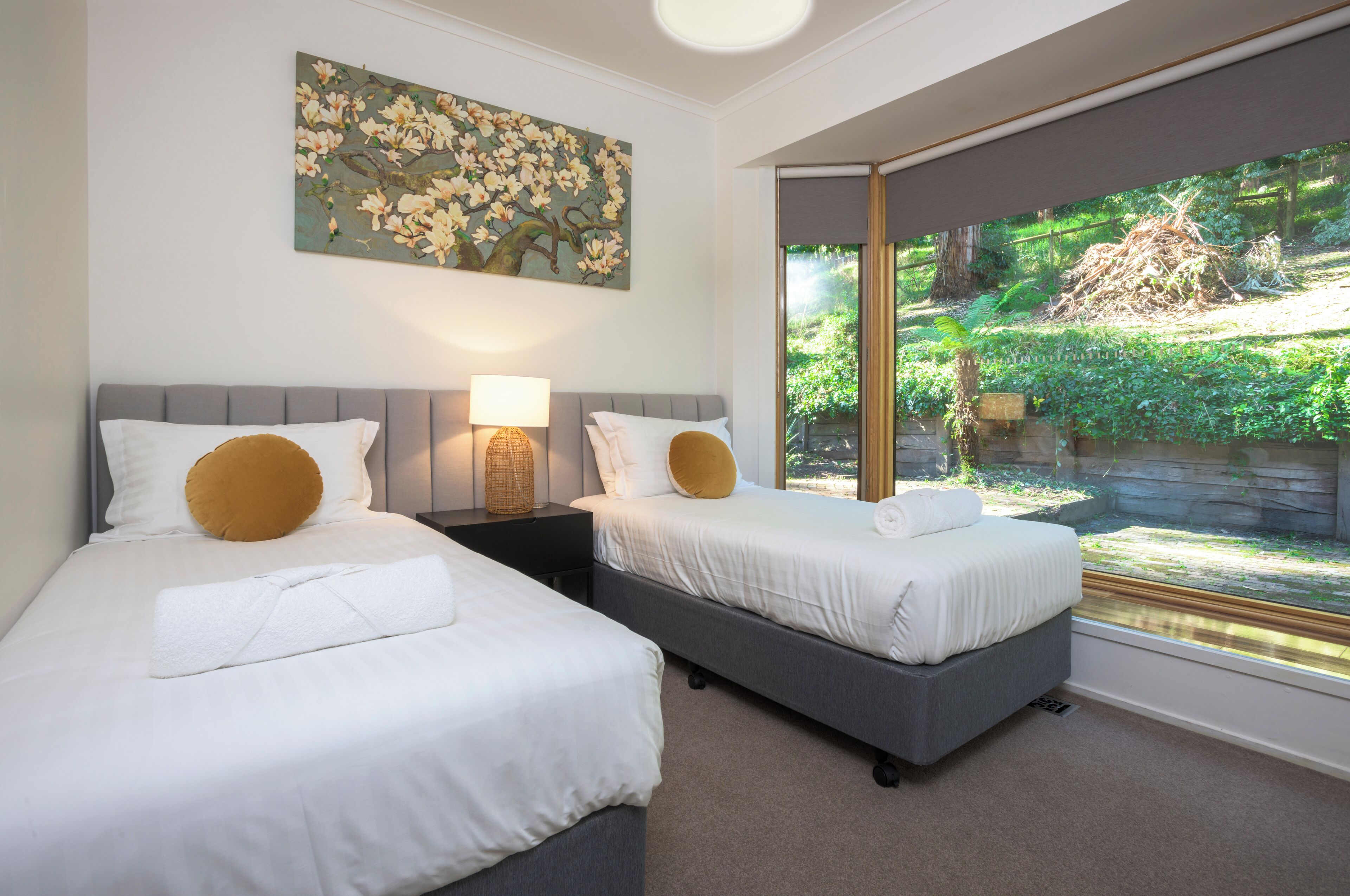 Quarto de hotel com duas camas, uma janela ampla com vista para área verde e um quadro na parede.