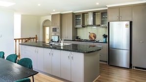 A modern kitchen with grey cabinets, a stainless steel refrigerator, and a wooden dining table with chairs. - Elliott Lodge - family & pet friendly (Upwey)