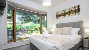 A bedroom with a large bed, a view of greenery through a sliding door, and a painting on the wall. - Elliott Lodge - family & pet friendly (Upwey)