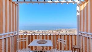 A balcony with a white table and two chairs, overlooking a coastal cityscape.