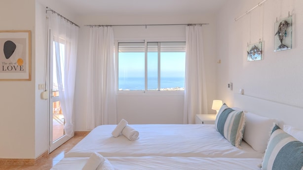 A hotel room with two beds, a large window with a view, a door with curtains, and a wall with framed artwork.