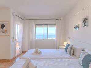 Camera d'albergo con due letti, una grande finestra vista, una porta con tende e un muro decorato con quadri.