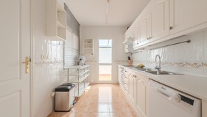 A narrow kitchen with white cabinets, a dishwasher, and a trash bin.