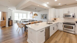 Una cocina moderna con armarios blancos, una isla central, electrodomésticos de acero inoxidable y una zona de comedor de madera.