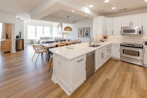 A modern kitchen with white cabinetry, a central island, stainless steel appliances, and a wooden dining area.