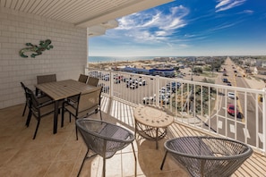 A balcony with a table and chairs, a view of a parking lot and buildings, and a clear sky.