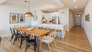 Una cocina moderna con armarios blancos, un refrigerador de acero inoxidable y una zona de comedor con una mesa y sillas de madera.