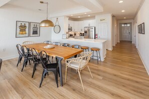 Una cocina moderna con armarios blancos, un refrigerador de acero inoxidable y una zona de comedor con una mesa y sillas de madera.