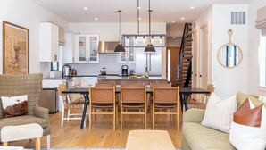 A modern kitchen with white cabinets, a central island, and pendant lighting. There is a staircase leading to an upper level. - Alpine House in Ketchum with Casita + Hot Tub (Ketchum)