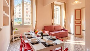 A dining area with a table set for four, a red sofa, and a city view through large windows. - Wonderful Apartment - Historic Center, Genova, Italy (Genova)
