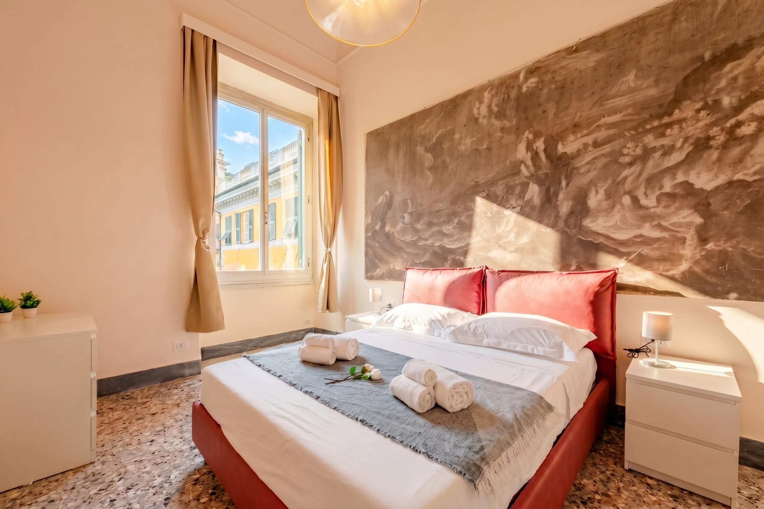 Una camera d'albergo con un letto, un comodino, una finestra con tende e un quadro astratto di grandi dimensioni sulla parete.