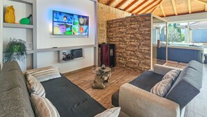A cozy living room with a stone wall, wooden ceiling, and a flat-screen TV mounted on the wall.