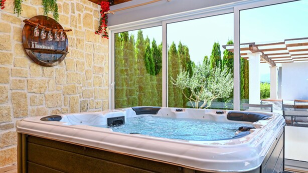 A hot tub with a stone wall backdrop and a large window overlooking a garden.