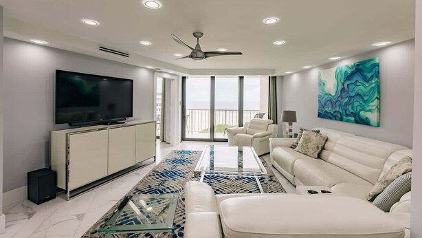 A modern living room with a flat-screen TV, white sofas, a glass coffee table, and a blue patterned rug. - Modern 2BR Condo l Gorgeous Oceanview (Marco Island)