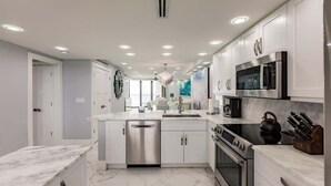 A modern kitchen with white cabinets, stainless steel appliances, and a marble countertop. - Modern 2BR Condo l Gorgeous Oceanview (Marco Island)