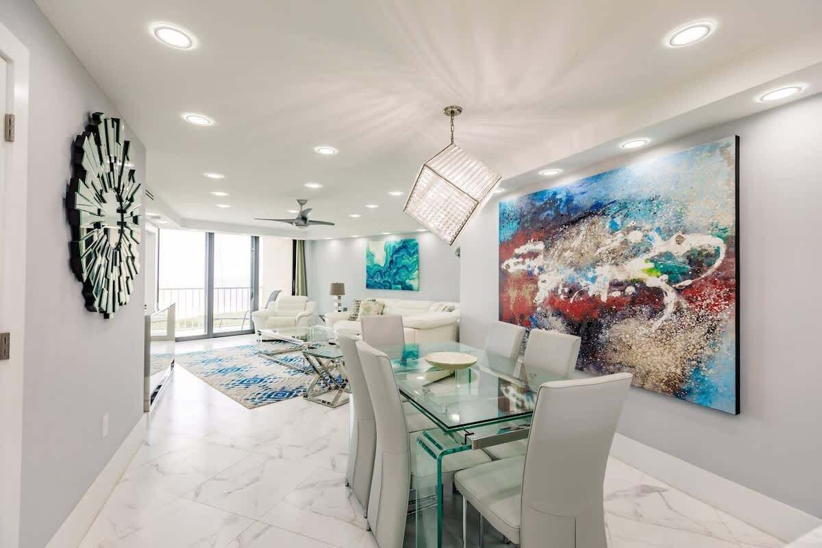 A modern dining area with a glass table, white chairs, and a large abstract painting on the wall.
