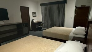 Ein Hotelzimmer mit zwei Betten, einem Schreibtisch, einem Stuhl, einem Fernseher und einem Fenster mit Vorhängen.