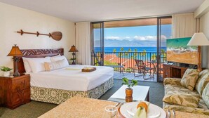 Een hotelkamer met een bed, een eettafel, een bank, een schilderij en een balkon met uitzicht op de oceaan.