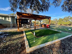 Un espace extérieur abrité avec des sièges, un barbecue et un petit terrain d’entraînement au golf.