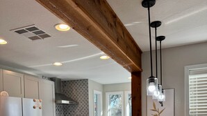 Eine Küche mit Kochinsel, Edelstahlgeräten, einem Holzbalken an der Decke und Pendelleuchten.