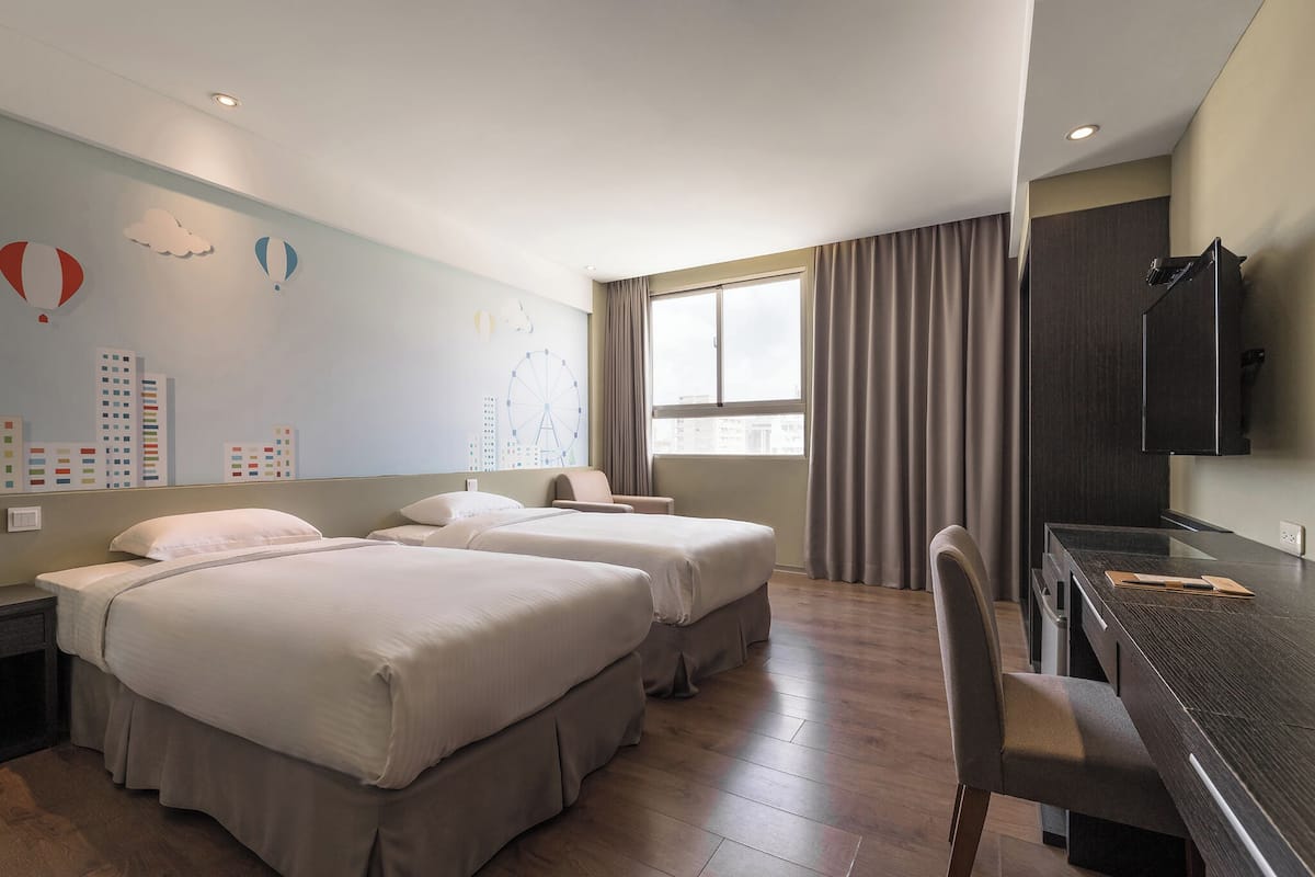 A hotel room with two beds, a desk, a chair, a TV, and a window with curtains.