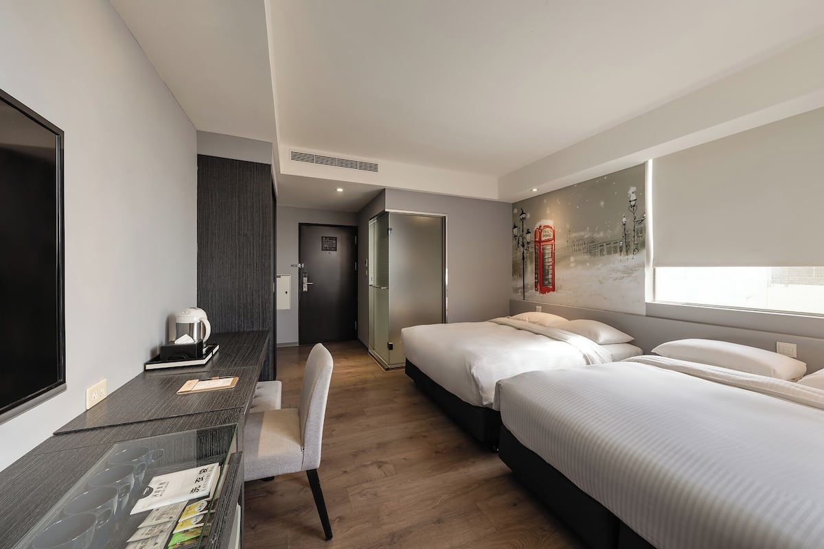 A hotel room with a bed, a desk with a coffee maker, a chair, and a large window.
