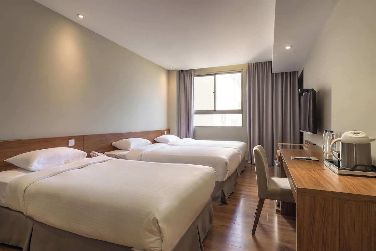 A hotel room with two beds, a desk, a chair, a coffee maker, and a TV.