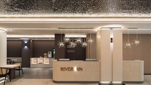 A modern reception desk with the name 'RIVER INN' in the center, a seating area with chairs and a table, and a patterned ceiling. - River inn ZihLi (Kaohsiung)