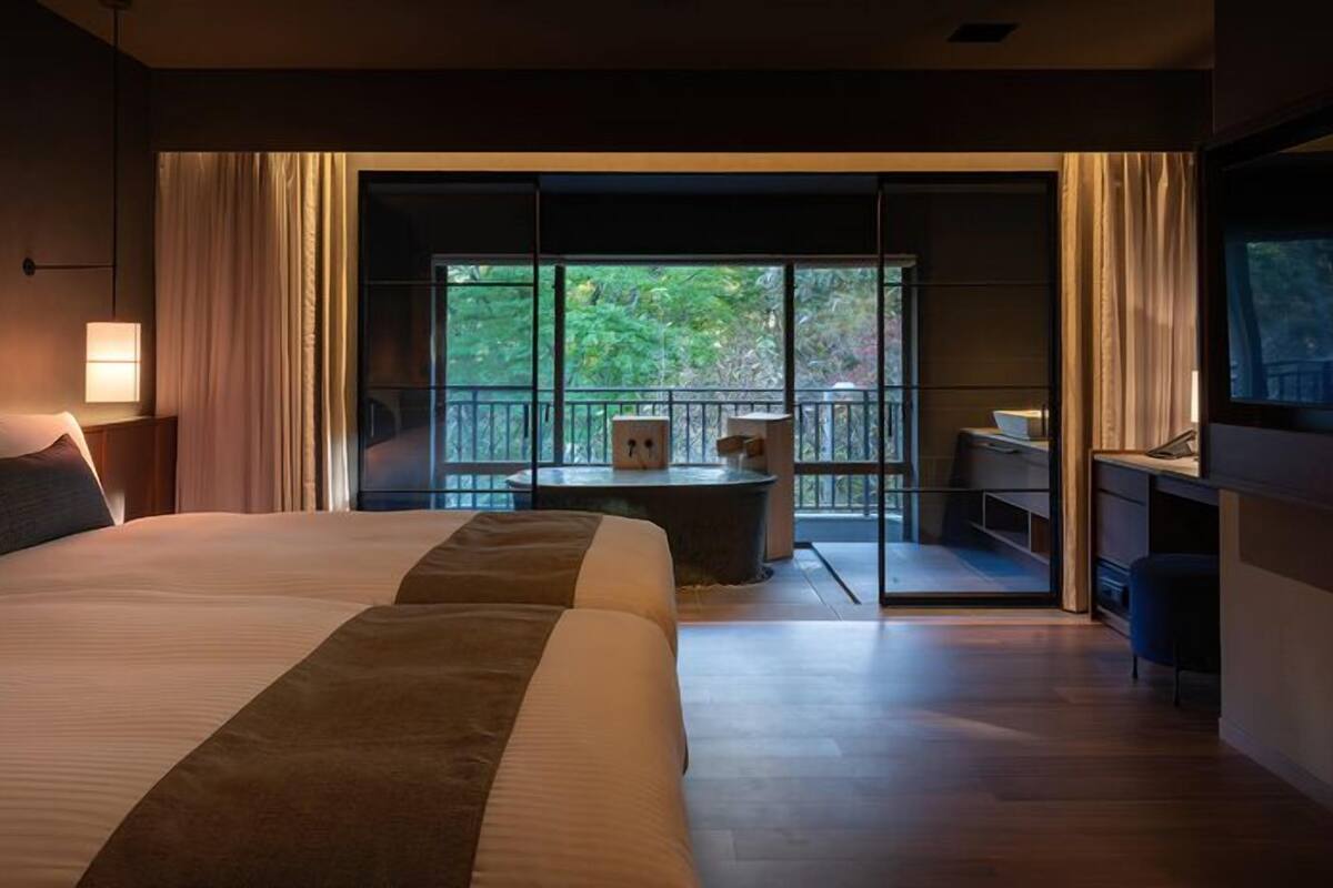 Habitación de hotel con una cama grande, un escritorio y un balcón con vistas a árboles.