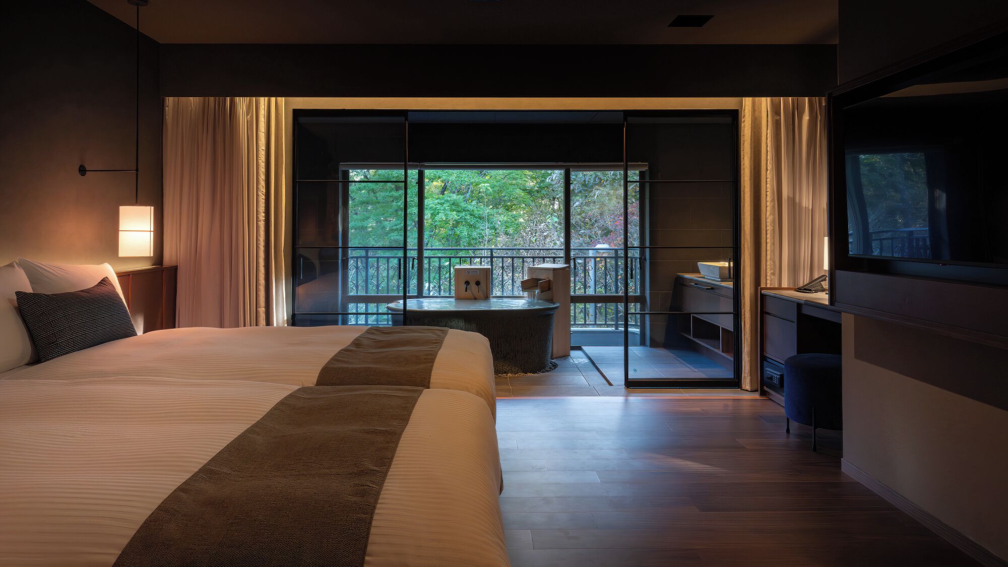 Une chambre d’hôtel avec un grand lit, un bureau, une chaise et un balcon donnant sur la verdure.