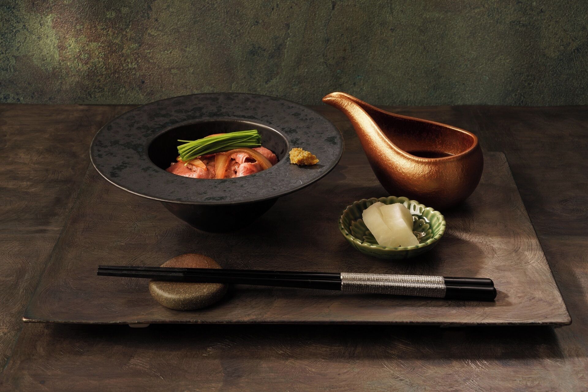 Un repas japonais traditionnel, composé d’un bol de nourriture, d’un pichet en cuivre et de baguettes, le tout disposé sur une table en bois.