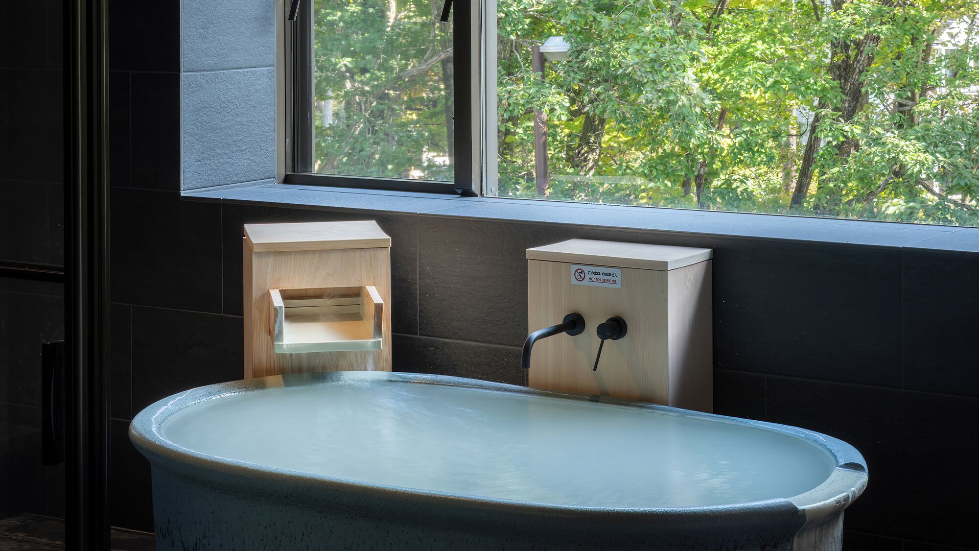 A bathtub with a wooden box and a sign, a window, and a view of trees.