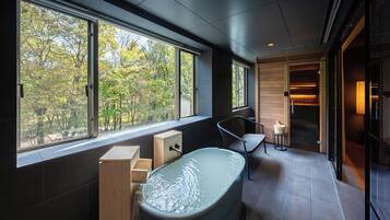 Un baño moderno con una bañera grande, armarios de madera y vistas a árboles a través de amplias ventanas.