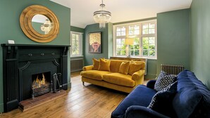 A room with a fireplace, a yellow sofa, a blue sofa, a chandelier, and a large window. - Lodge Farm - Stunning 3 BD with Garden (Oxford)