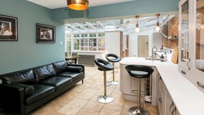 A modern kitchen with a large island, bar stools, and a hanging light fixture. - Lodge Farm - Stunning 3 BD with Garden (Oxford)