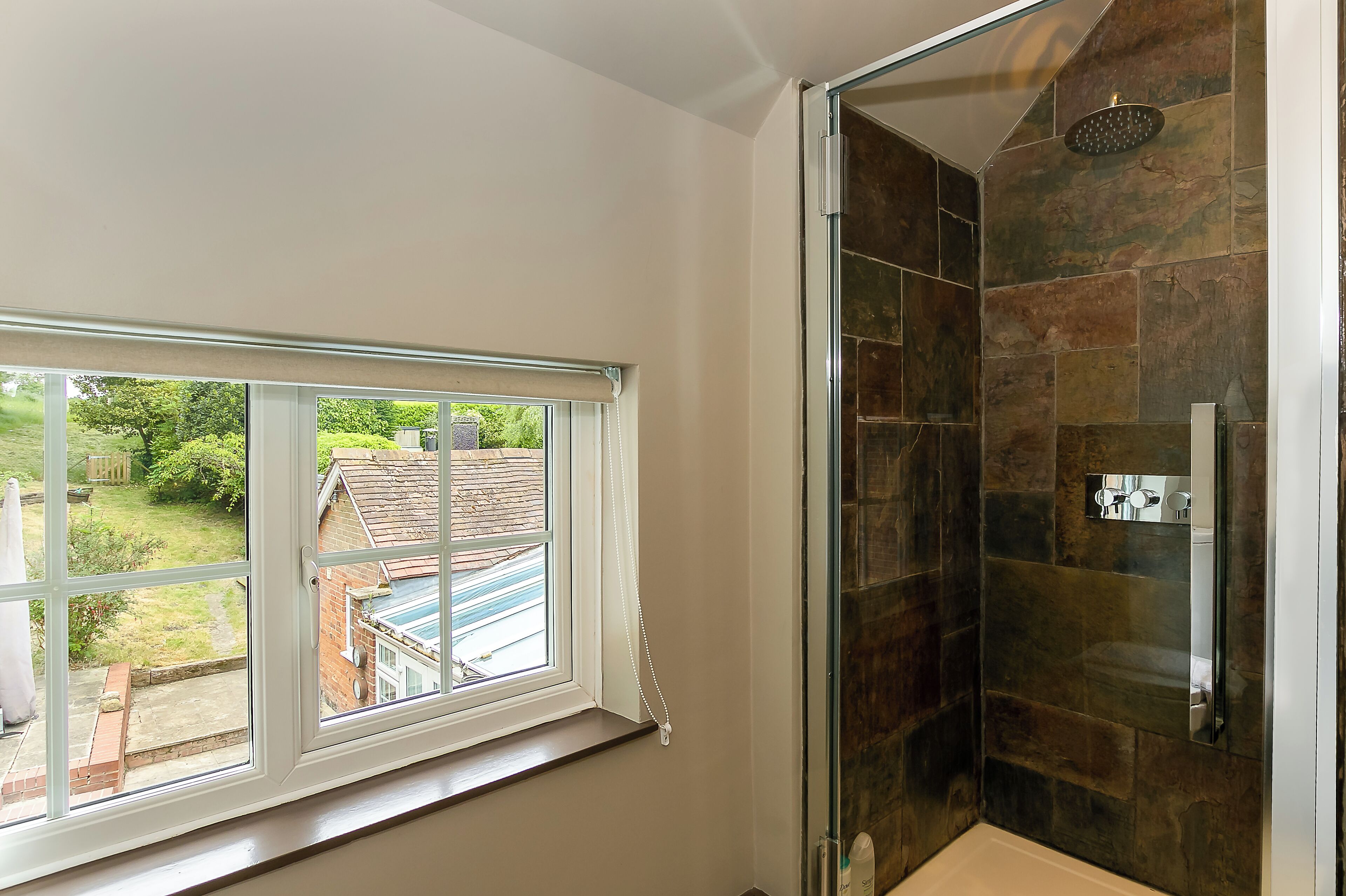 A bathroom with a glass shower enclosure and a window overlooking a garden.