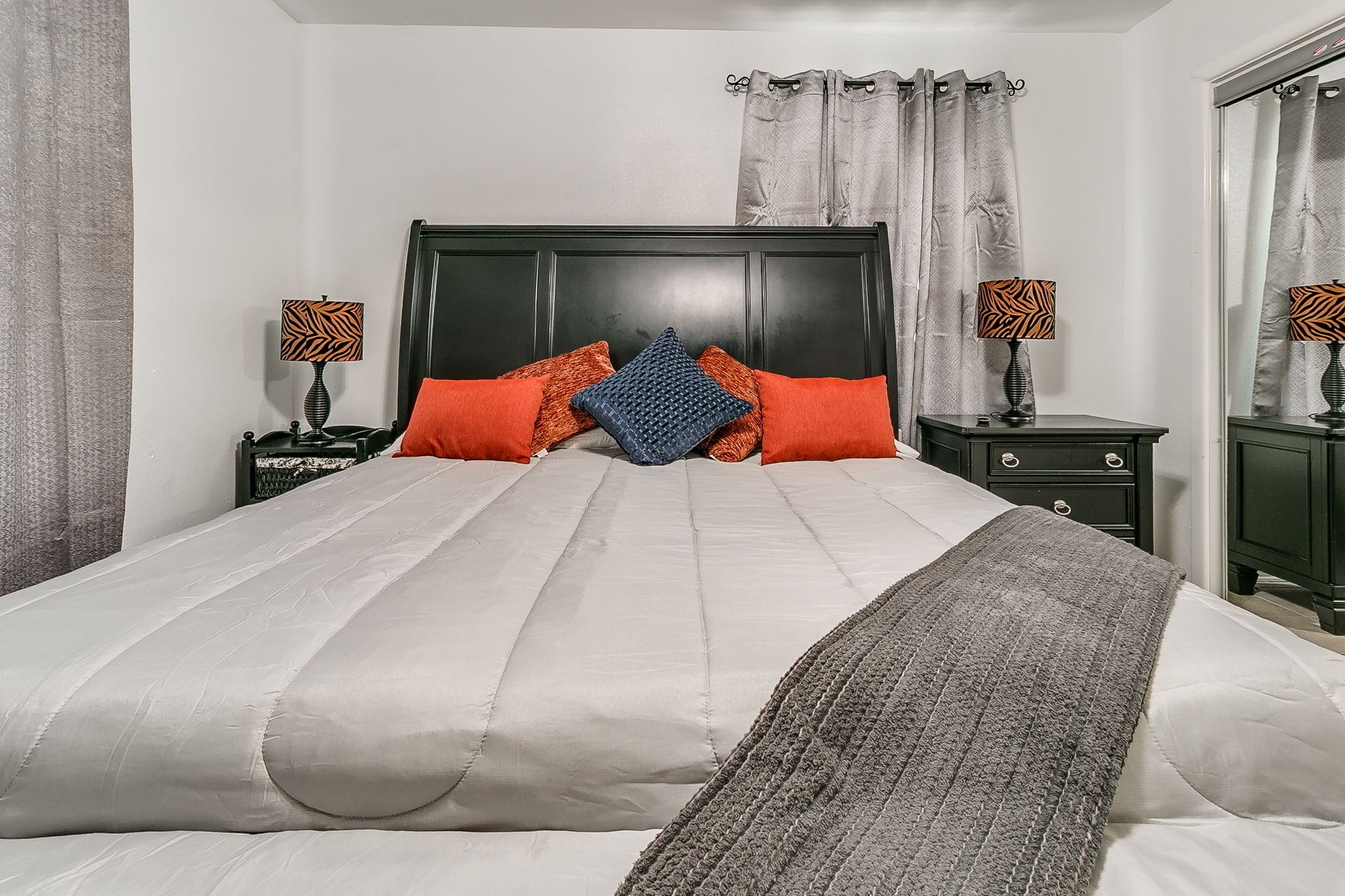Cama bem arrumada com cabeceira, duas mesinhas de cabeceira com luminárias e um espelho na parede.