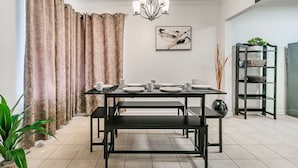 A dining area with a table set for four, a chandelier, a wall-mounted abstract painting, and a shelving unit with baskets.