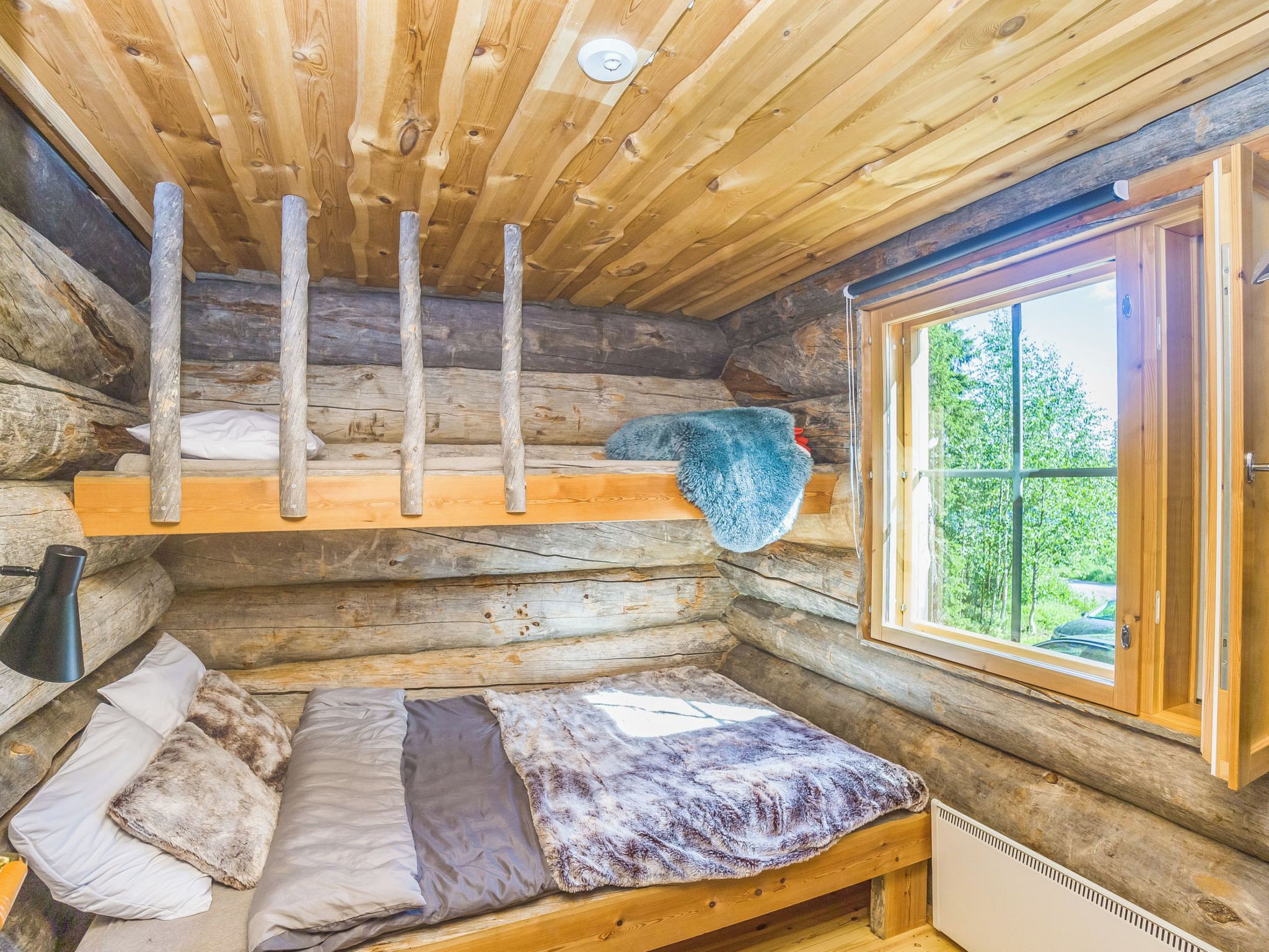 A log cabin room with a loft bed, a window with a view, and a heater.