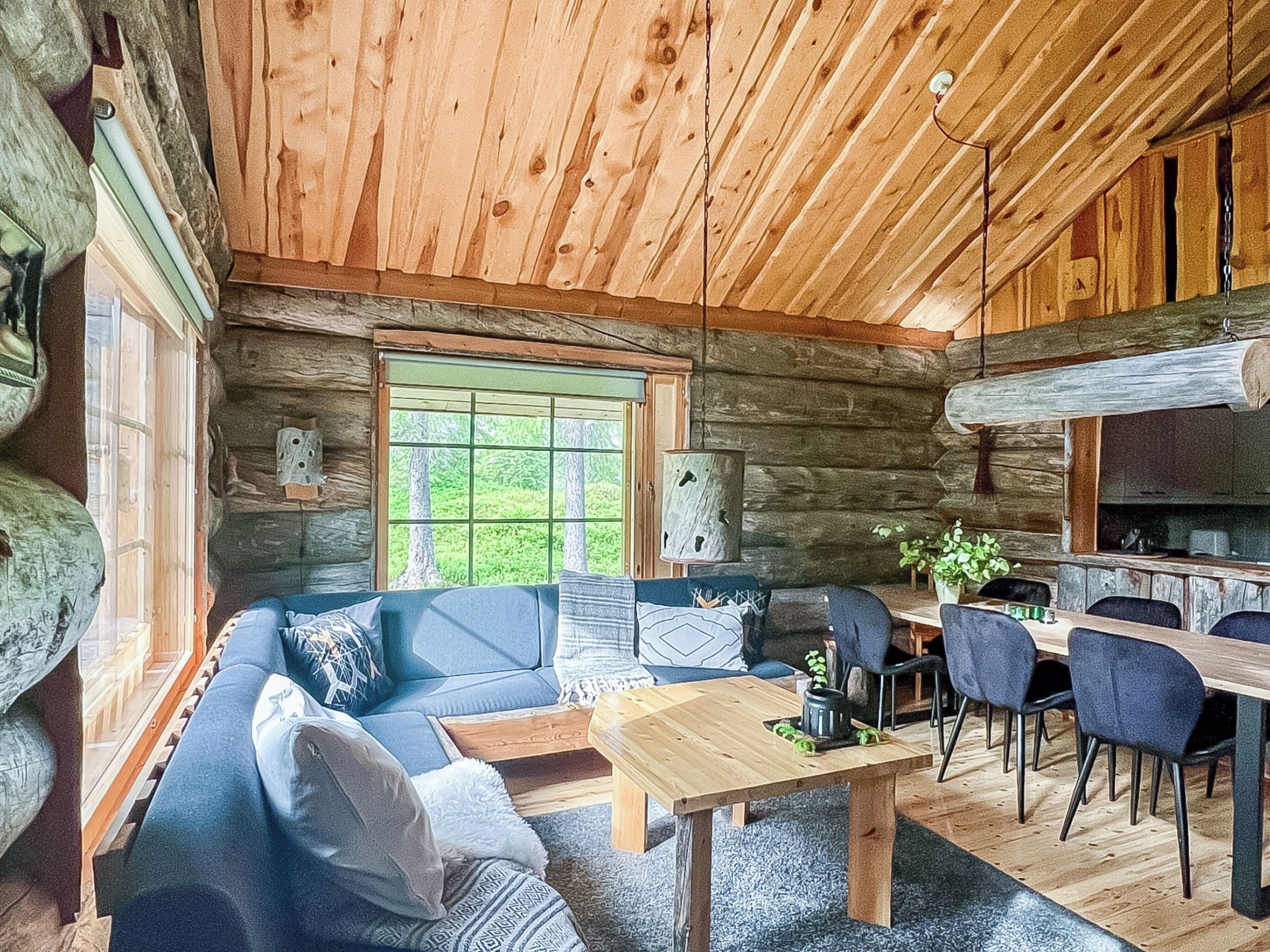 A log cabin interior with a sofa, dining table, chairs, and a large window.
