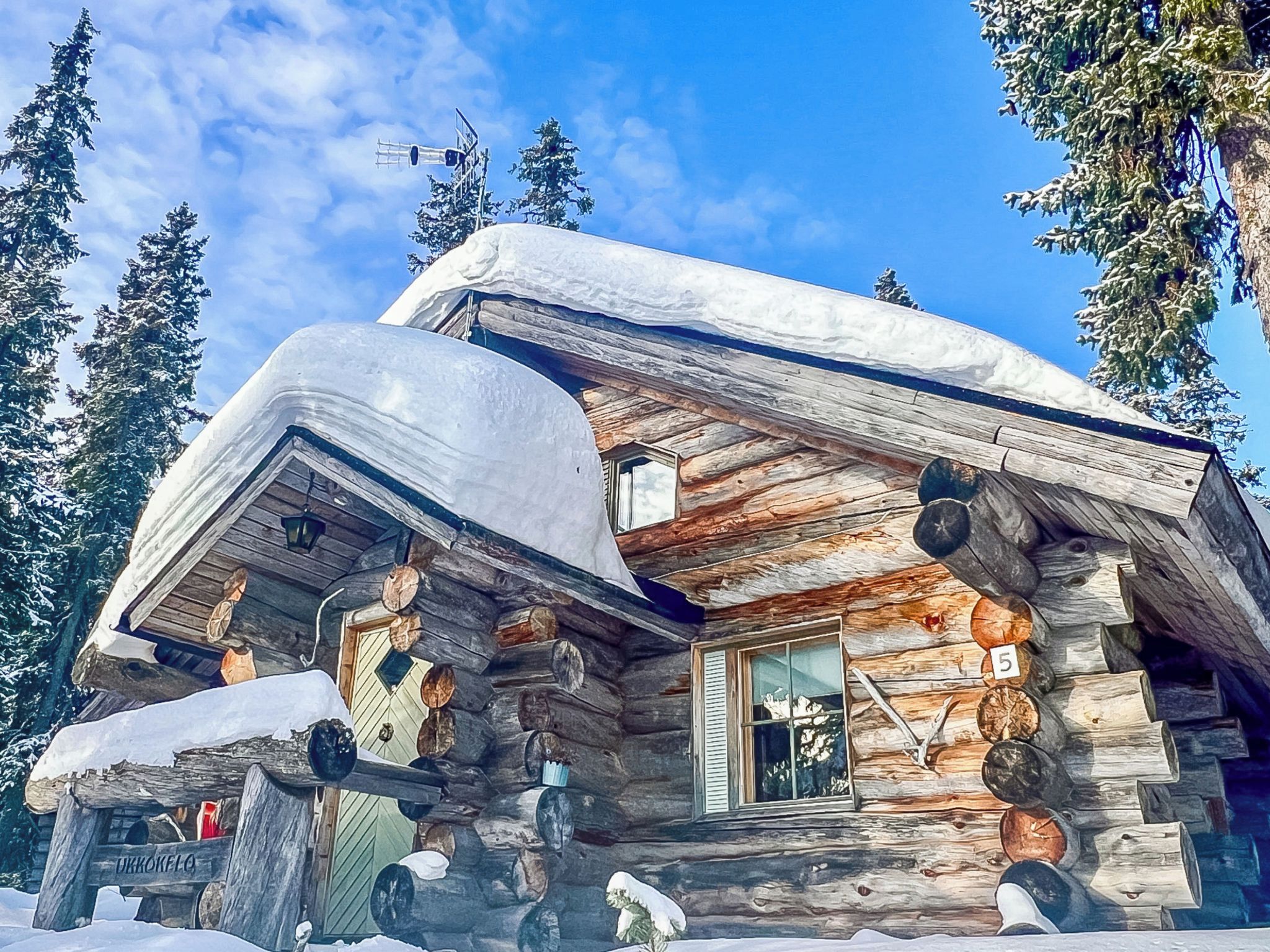 A log cabin with a snow-covered roof, wooden walls, and a window with shutters.