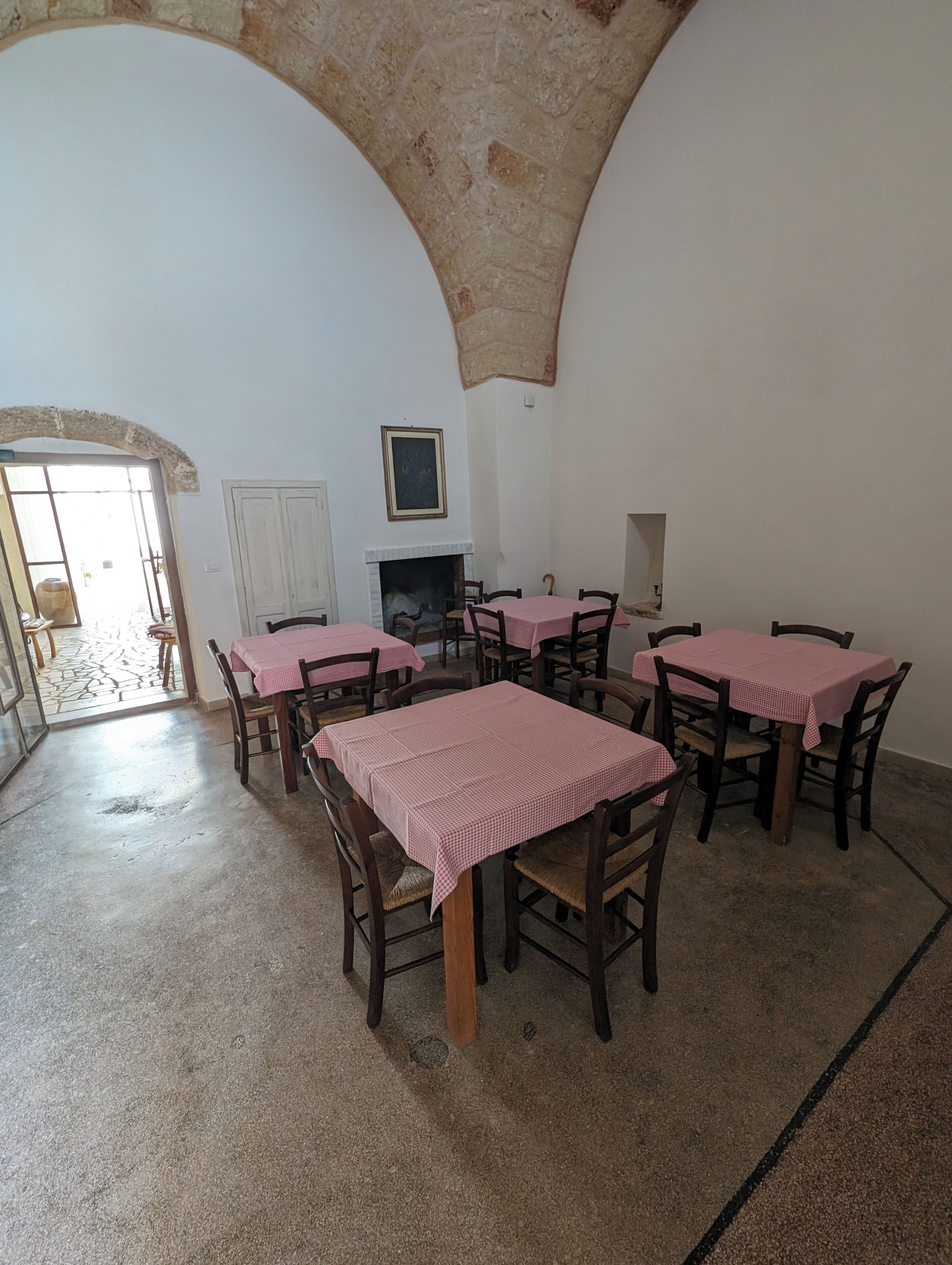 Un comedor con varias mesas cubiertas de manteles a cuadros, sillas de madera y un arco de piedra.