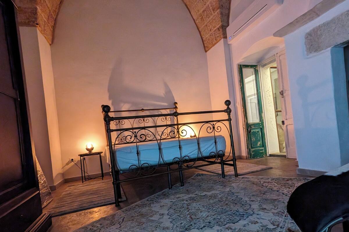 Une chambre à coucher avec un lit, un tapis et une arche en pierre.