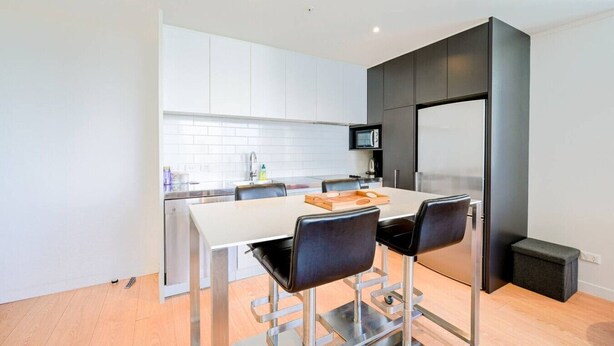 A modern kitchen with a white countertop, black chairs, and a stainless steel refrigerator.
