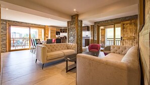 Un vaste espace de vie comprenant un grand canapé, un fauteuil rouge et une table basse. On peut y admirer un pilier en pierre et des éléments décoratifs en bois.