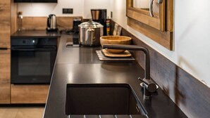 Une cuisine moderne dotée d’un plan de travail noir, d’un évier en acier inoxydable, de meubles en bois et d’un four encastré.