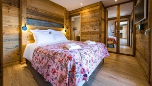 Une chambre à coucher aux murs lambrissés, avec un lit, deux lampes fixées au mur et un mur d’accent en pierre.
