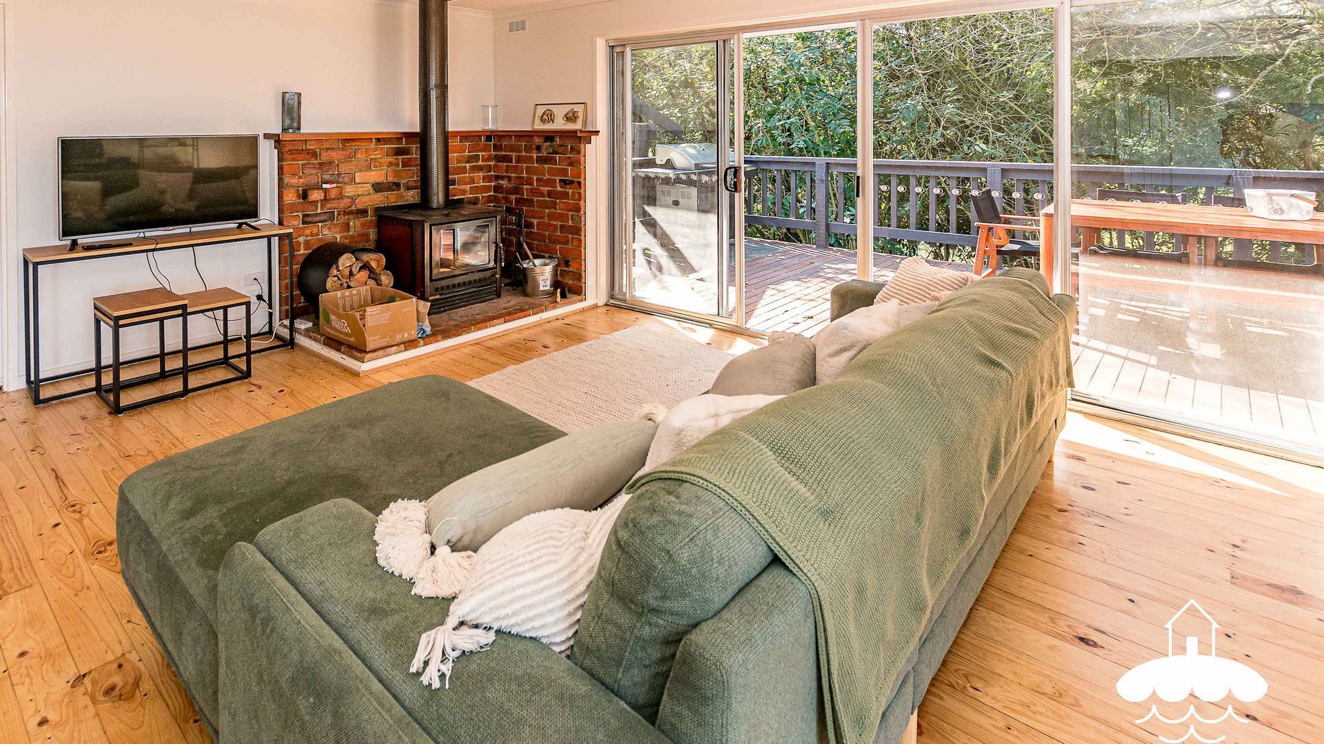Un salon avec un canapé vert, un téléviseur, une cheminée et un balcon aménagé avec du mobilier d’extérieur.