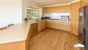 Une cuisine moderne avec des meubles en bois, un réfrigérateur en acier inoxydable et une grande fenêtre qui laisse entrer la lumière naturelle.